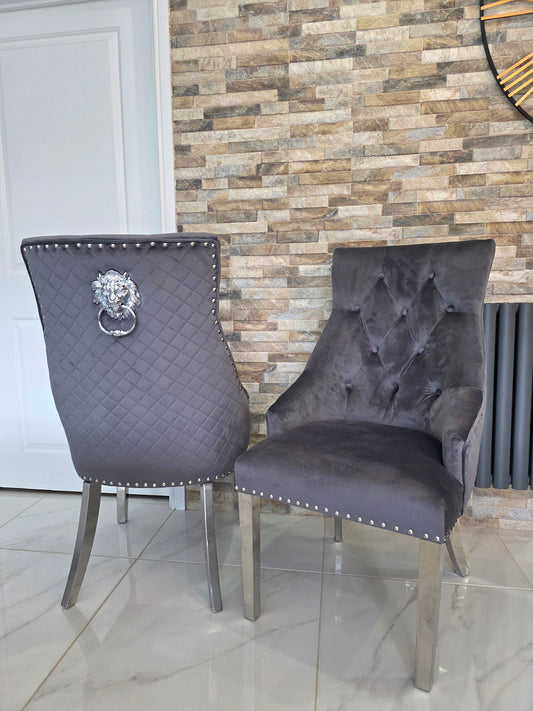 Two gray upholstered chairs with lion knocker backs in a room with a stone wall.