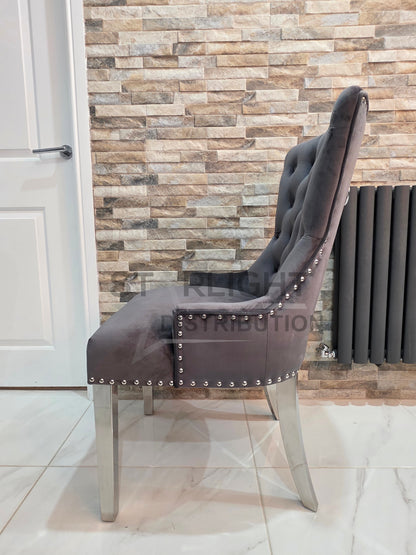 Gray upholstered chair with nailhead trim against a stone wall.